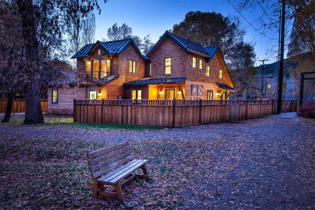 A warm wooden home and its fenced backyard aglow at night